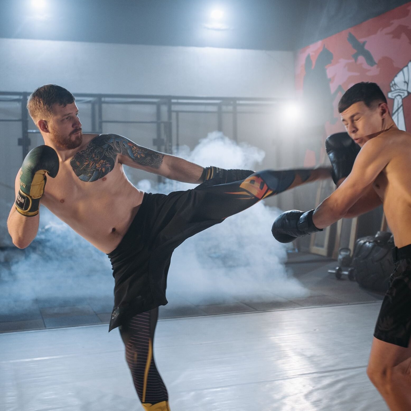 Two shirtless men engaging in vigorous MMA sparring, demonstrating skill and intensity indoors.