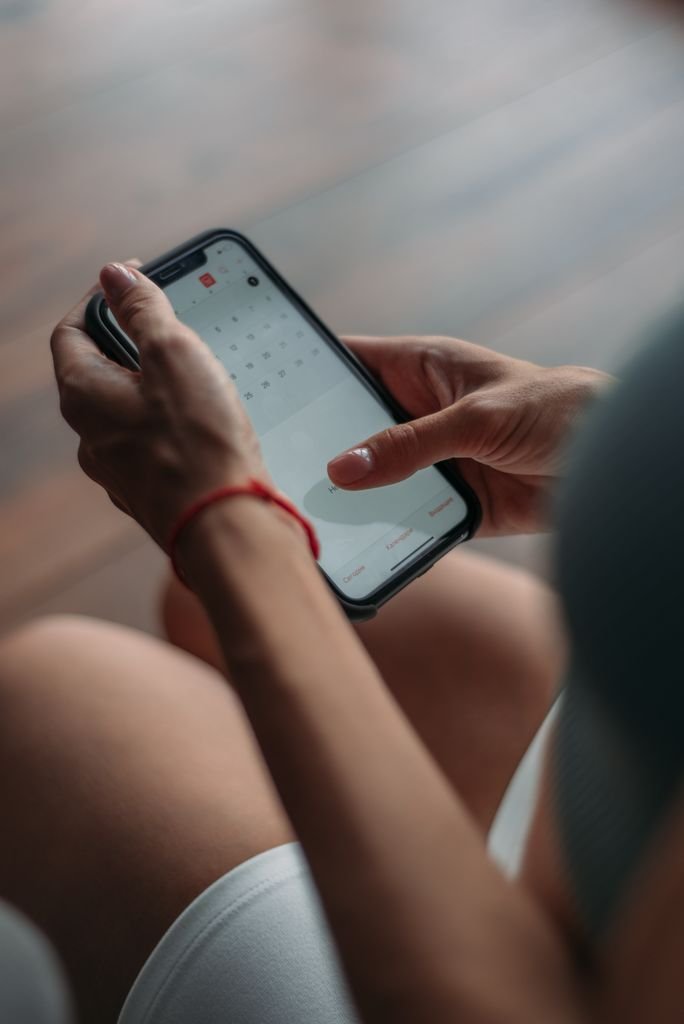 Close-up of a person using a smartphone to access the calendar app indoors.